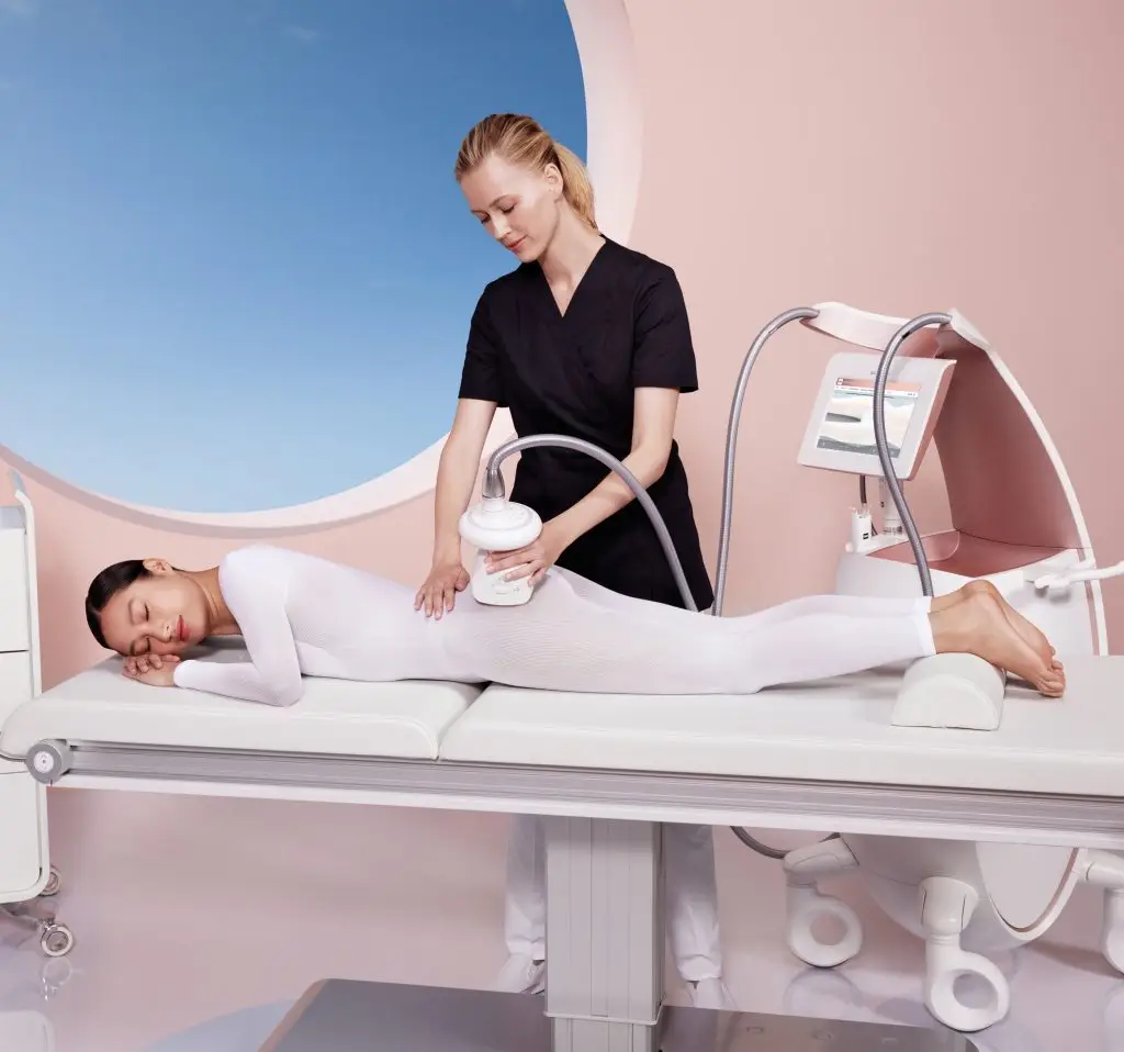 Endermologie specialist applying body sculpting device to woman lying on table